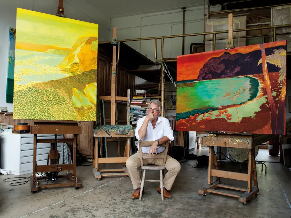 Jeroen Krabb&eacute; zit in zijn atelier, omringd door zijn kleurrijke landschapsschilderijen.