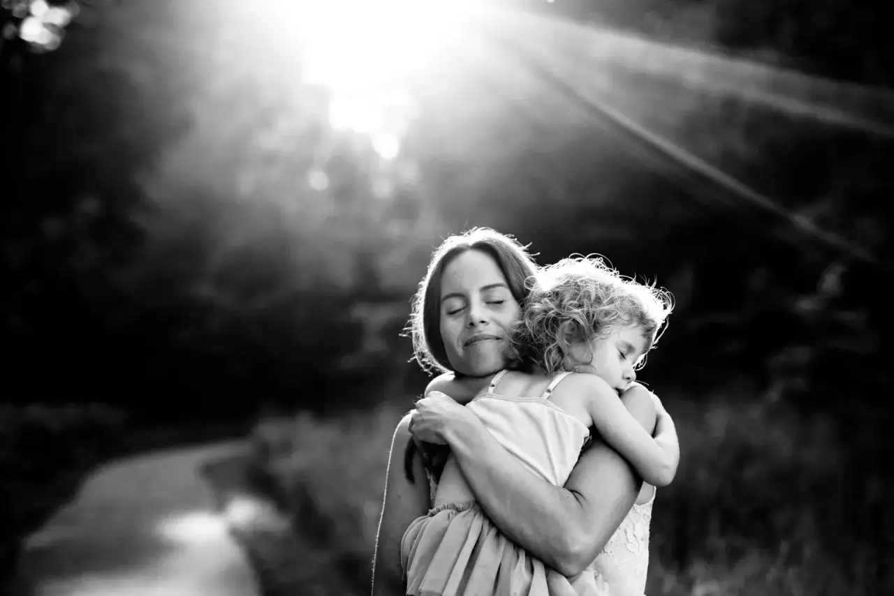 Zwart-wit fotograaf legt een moeder vast die haar slapende kind omhelst, badend in zacht zonlicht. Een moment van pure liefde.