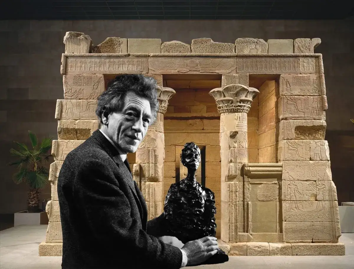 Een man met een donkere jas staat voor een Egyptische tempel, met een beeldje in zijn handen. Alles is op schaal.