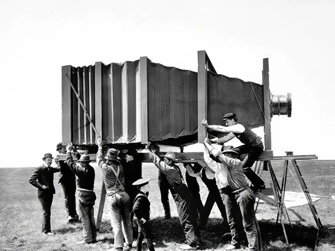 Mannen met hoeden tillen een gigantische camera, mogelijk de eerste camera ooit, op een statief.