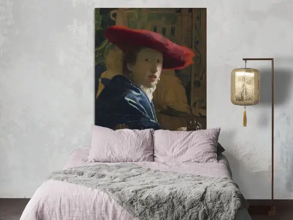 Een meisje met de rode hoed, geschilderd door Vermeer, kijkt mysterieus vanaf de muur boven een zachtroze bed.