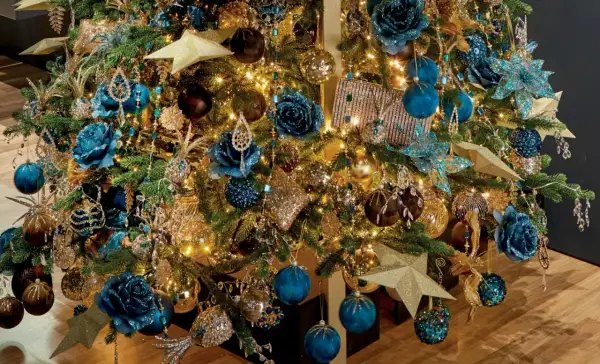 Een kerstboom vol met blauw goud, glinsterende ornamenten, blauwe bloemen en gouden sterren.