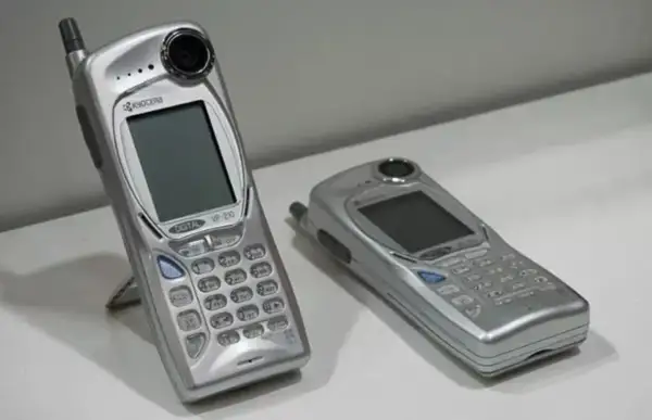 Twee zilverkleurige mobieltjes, waaronder de Kyocera VP-210, de eerste telefoon met camera.