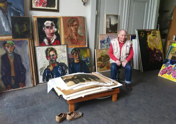 Jan Sierhuis, omringd door zijn kleurrijke portretten en stadsgezichten, in zijn atelier.