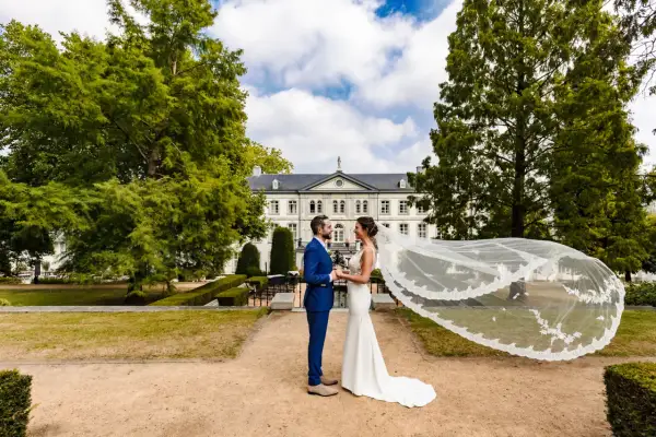Bruidspaar geniet van hun fotoshoot kasteel. De bruid draagt een witte jurk met sluier, de bruidegom een blauw pak.