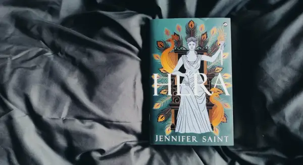 Boek "Hera" van Jennifer Saint, met de godin Hera afgebeeld met pauwenveren en een fakkel.