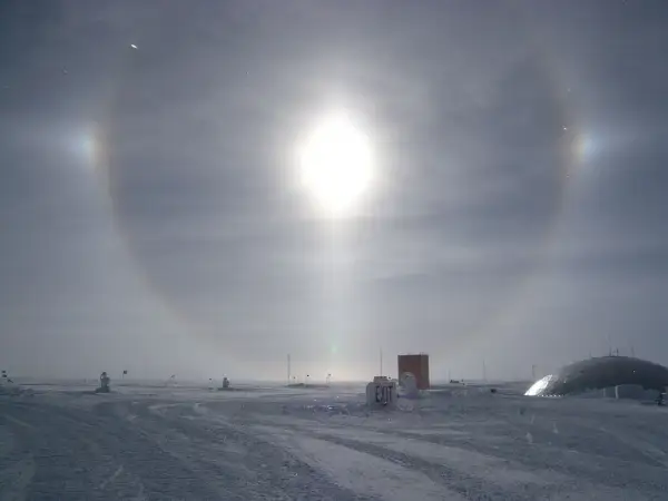 Een spectaculaire halo effect zon boven een besneeuwd landschap met gebouwen en vlaggen.